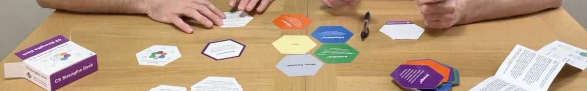 Game pieces and cards on a table with players' hands, indicating a game in progress.